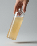 Hand holding a glass bottle with a yellow liquid against a gray background